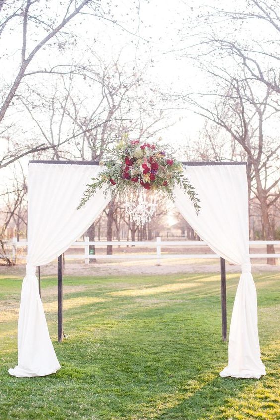 outdoor wedding ceremony arbor, ruby red flowers, draped white fabric, chandelier