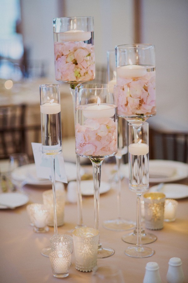 Clusters of stemmed hurricane vases filled with floating candles and rose petals
