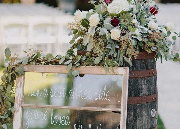 bohemian wedding decorations signs on old window frame near with wine barrel and red flowers