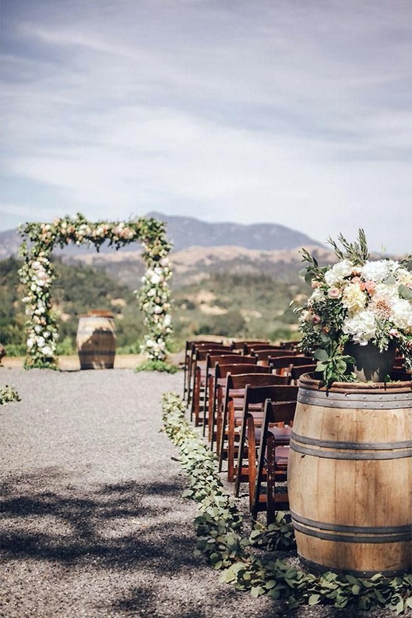 rustic wedding decor outdoor ceremony with wine barrel flowers and greenery arch