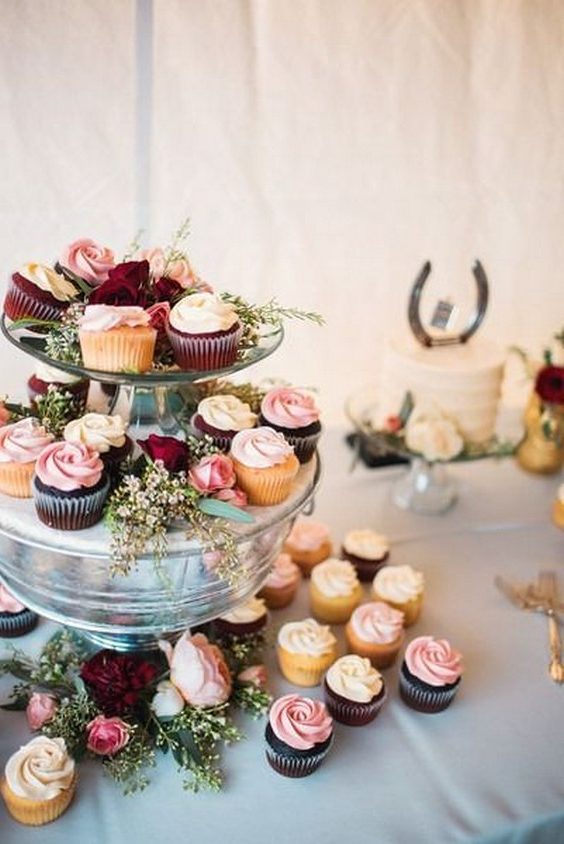 Wedding cupcake display- assorted cupcakes with ivory + pink frosting on clear tower with greenery + flowers