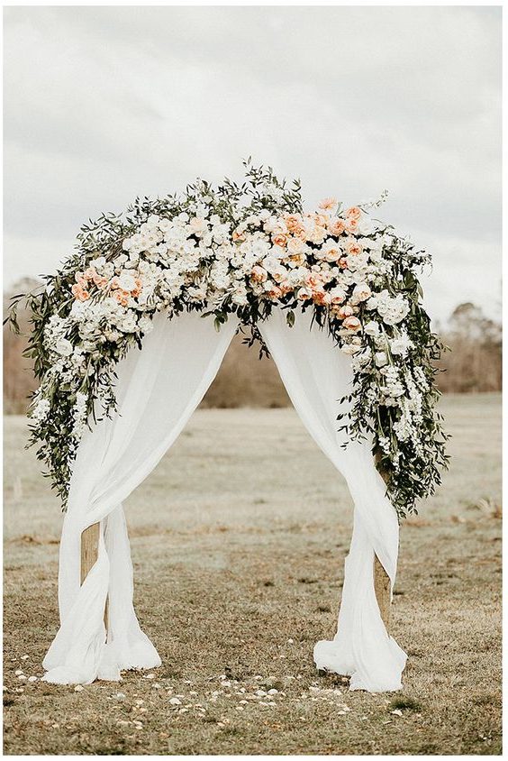 floral wedding arch with white and peach flowers, greens and draped fabric