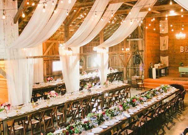 Rustic barn wedding reception space with draped white fabric decor