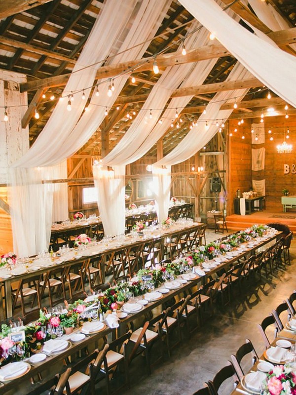 Rustic barn wedding reception space with draped white fabric decor