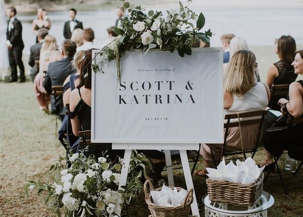 romantic beach wedding ceremony welcome sign with green and white flowers and petal cones