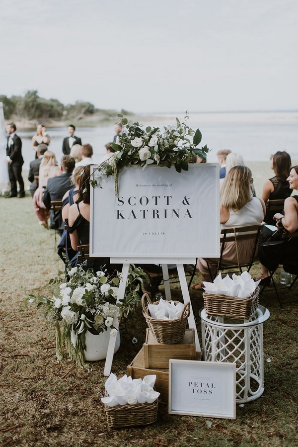 romantic beach wedding ceremony welcome sign with green and white flowers and petal cones