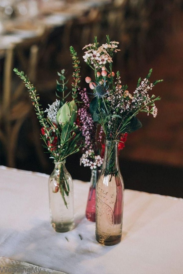 Rustic wildflower wedding centrepiece in mixed vintage bottles