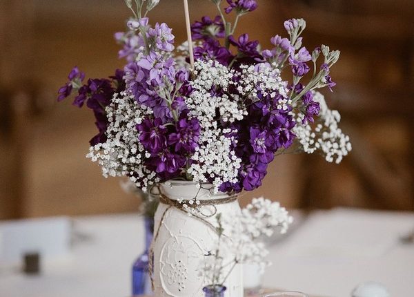 White mason jar centrepiece with purple and white flowers and a burlap table number.