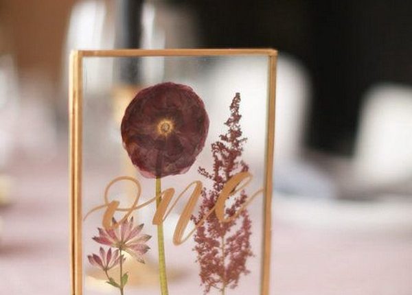 table numbers make of pressed flowers in a frame reading “one” in gold calligraphy